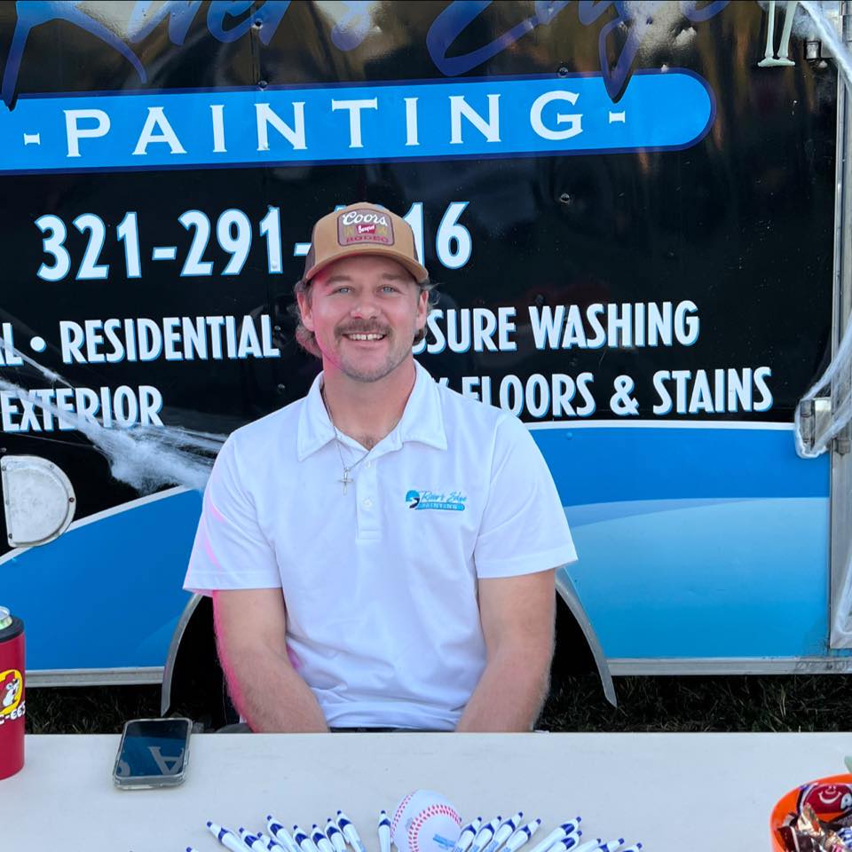 Jake, owner of Rivers Edge Painting, at the company booth with the Rivers Edge Painting trailer at a local Space Coast event